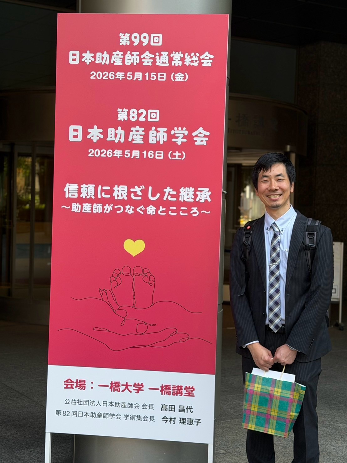 第82回日本助産師学会の看板の横で笑顔を見せる有路登志紀